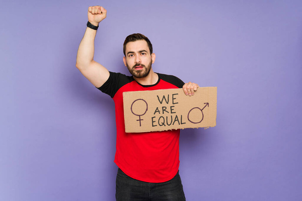 Studio shot of a man in his 30s holding up a protest sign and raising his arms to support gender equality - Foto, imagen