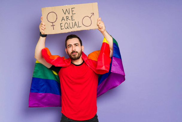 Atractivo hombre queer con una bandera arcoíris que apoya los derechos de los homosexuales y la igualdad de género en una marcha LGBT  - Foto, Imagen