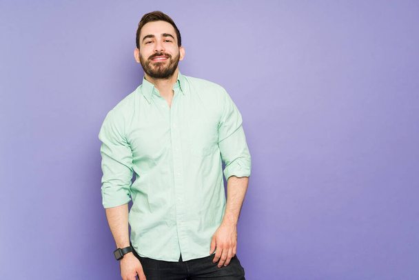 Handsome man in his 30s feeling positive and happy while posing against a purple background with copy space - Фото, изображение
