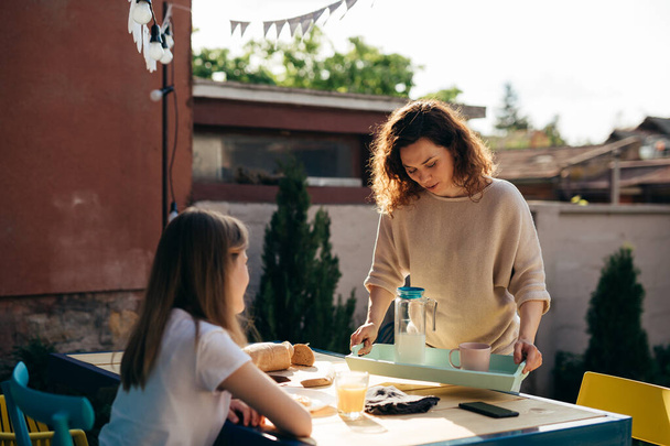 caucasian mother brings food to the table for breakfast in backyard - Фото, изображение