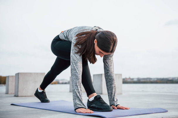 Giovane ragazza sportiva che fa esercizi di yoga sul tappeto fitness all'aperto vicino al lago durante il giorno. - Foto, immagini