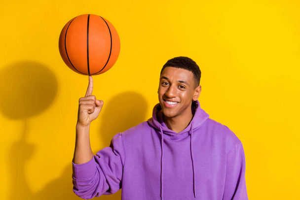 Portrét atraktivní veselý sportovní chlap točení na ukazováčku oranžová koule izolované přes jasně žluté barvy pozadí - Fotografie, Obrázek
