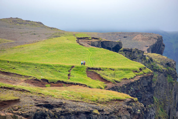 Two people are walking along the mountain green slope of Iceland. Travel and tourism - 写真・画像