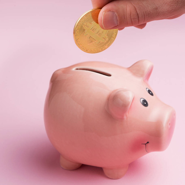 αρσενικό χέρι βάζει Bitcoin κέρμα σε ένα ροζ κουμπαρά, χρηματοδότηση και cryptocurrency έννοια - Φωτογραφία, εικόνα