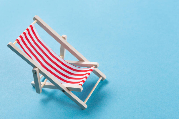 single empty chaise lounge with red striped cloth laid out on a blue background, vacation concept, copy space - Photo, Image