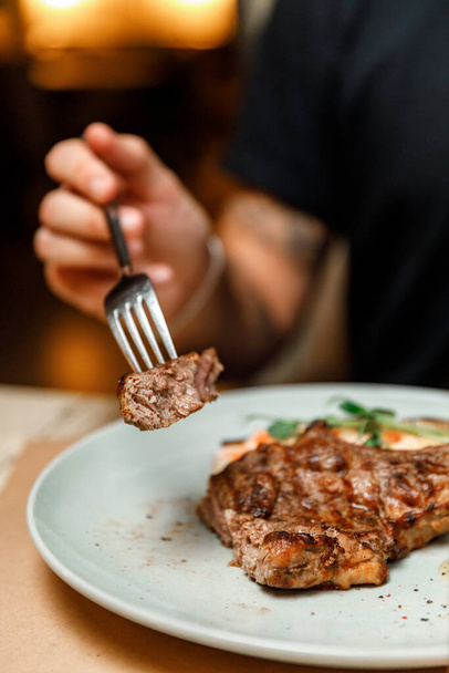 dish plate with meat steak on the bone in the restaurant. man cuts ready juicy meat steak - Φωτογραφία, εικόνα