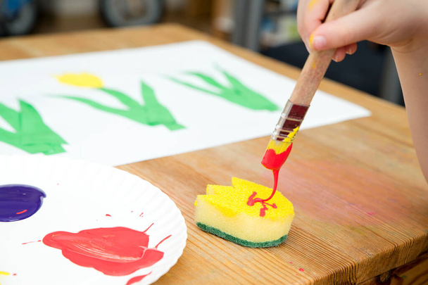 Kid painting with gouache a spring flower. Boy produces colored tulips for mommy. Children's activities, easy ideas for children at home. Art lessons at home. DIY tasks for children. Early education. - Photo, Image