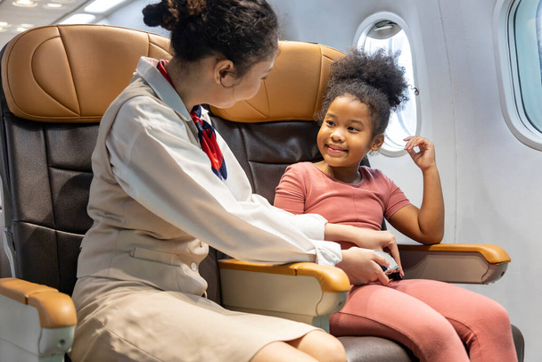 客室乗務員は離陸前に飛行機に安全手順として搭乗した後、若いアフリカ系アメリカ人の子供のためのシートベルトを固定するのを助けます - 写真・画像