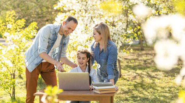klein meisje met mam en pap studeren op laptop outdoor - Foto, afbeelding