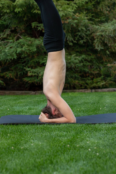 Vertical view of young man in sirasana pose while practising yoga in th natural air in the garden - Fotoğraf, Görsel