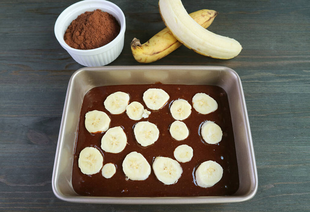 Pastella di torta di banana al cioccolato fondente fatta in casa in padella con ingredienti di cottura sulla tavola di legno - Foto, immagini