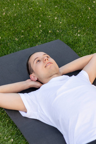 Молодий чоловік насолоджується відпочинком в саду, дивлячись на чисте небо на білій футболці в парку
 - Фото, зображення
