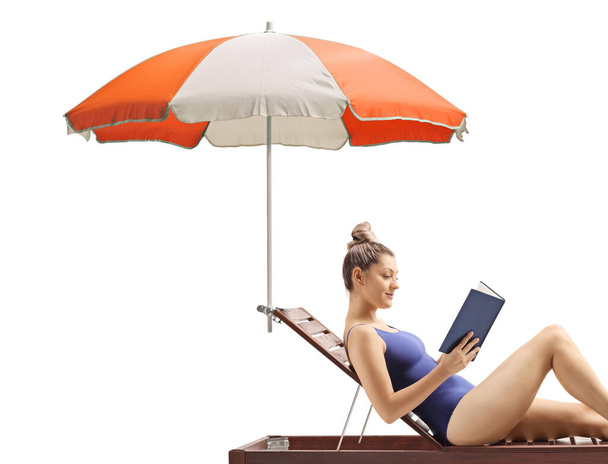 Woman reading a book and relaxing on a sunbed under umbrella isolated on white background - 写真・画像