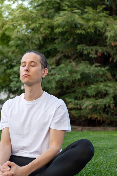 Young man with eyes closed taking deep breath from fresh and clean air sorrounded by nature in a park - Foto, Bild