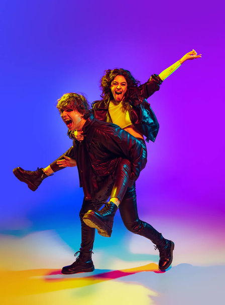 Young couple of rock-and-roll musicians wearing black leather outfits gesturing, shouting and posing on blue yellow background in neon light - Foto, imagen