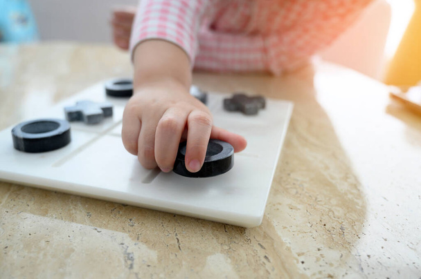Primo piano mano di bambino bambina che gioca Tic Tac Toe o OX gioco da tavolo sul tavolo di marmo, vista dall'alto - Foto, immagini