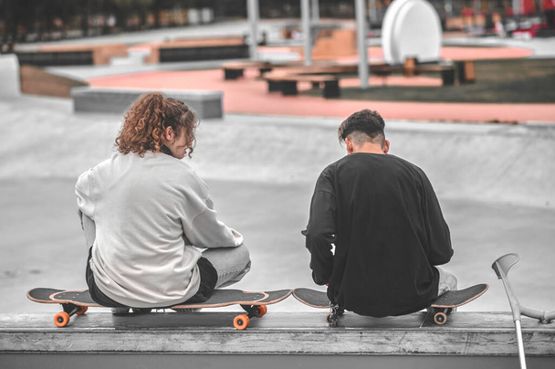 Back view of girl and guy sitting on skateboards - Foto, Imagem