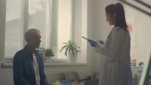 Doctor consulting sick senior patient using tablet in hospital. - Video, Çekim