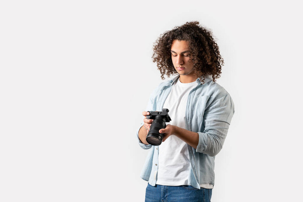 Young man with curly hair is holding a camera on his hand. Hobby and photography concept. - Foto, imagen