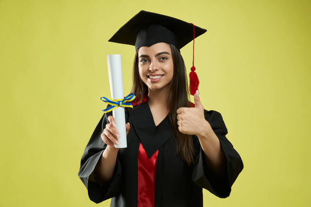Girl in mortarboard and graduate gown holding diploma. - Фото, зображення