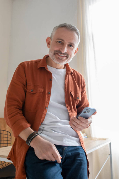 A gray-haired man in orange shirt looking happy - Foto, afbeelding