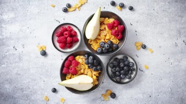 Golden cornflakes with fresh fruits of raspberries, blueberries and pear in ceramic bowl - Footage, Video