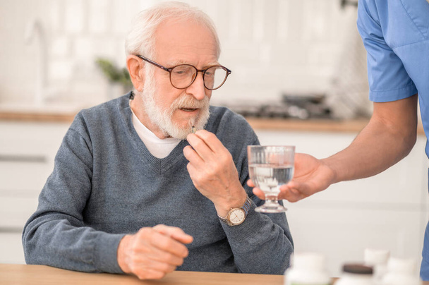 Pensioner taking a medicine under the supervision of his nurse - Фото, изображение