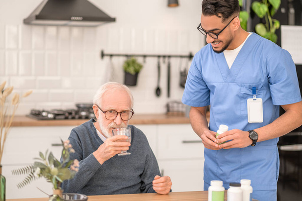 Young healthcare worker observing a pensioner swallowing down a medication - Foto, imagen
