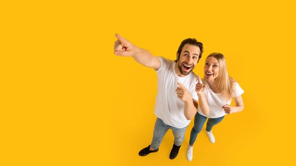 Glad surprised excited millennial caucasian husband and wife in white t-shirts pointing up at empty space - Foto, imagen