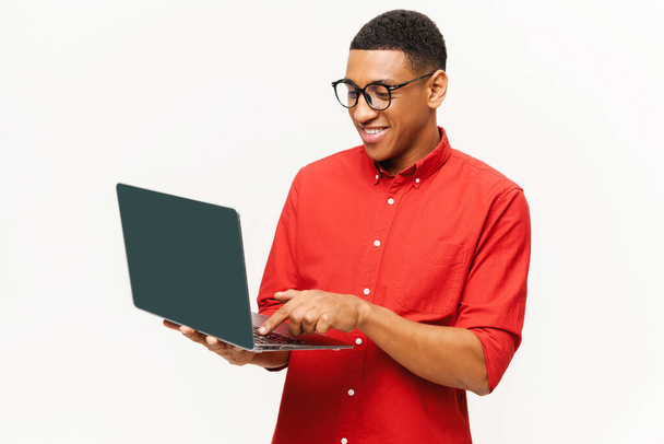 Cheerful handsome smiling African-American young man in red shirt using laptop isolated on white - Φωτογραφία, εικόνα