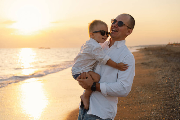 Father and baby play on the beach. Dad and him Child together enjoying sunset. - Photo, Image