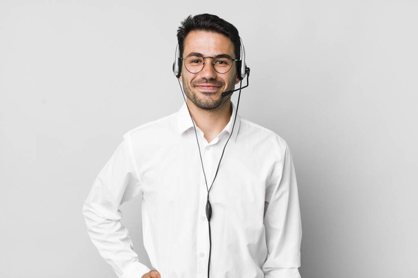 young adult hispanic man smiling happily with a hand on hip and confident. telemarketer concept - Foto, Imagem