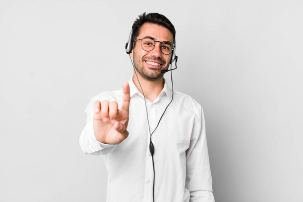 young adult hispanic man smiling proudly and confidently making number one. telemarketer concept - Foto, Imagen