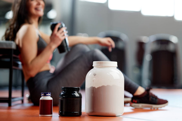 Selective focus on supplements and protein power in gym with a sportswoman. - Foto, imagen