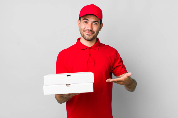 young adult hispanic man smiling cheerfully, feeling happy and showing a concept. pizza delivery concept - Foto, afbeelding