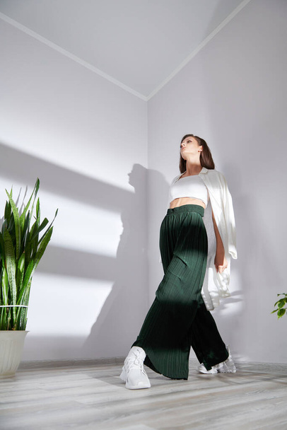 modèle dans des vêtements élégants modernes posant pour un photographe sur un mur blanc - Photo, image