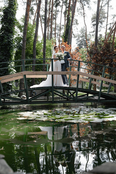 A wedding couple on a bridge over a lake with red fish in the woods. - Photo, Image
