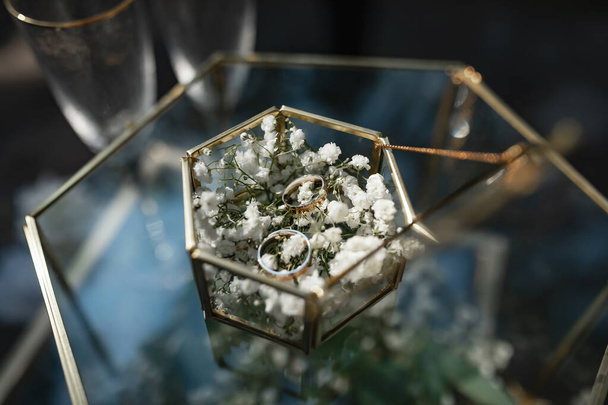 Anelli in oro nuziale si trovano in una scatola di vetro decorata con fiori. - Foto, immagini