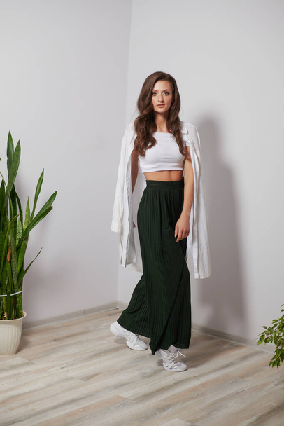 girl in green pants and a white shirt posing on a white wall - Fotoğraf, Görsel