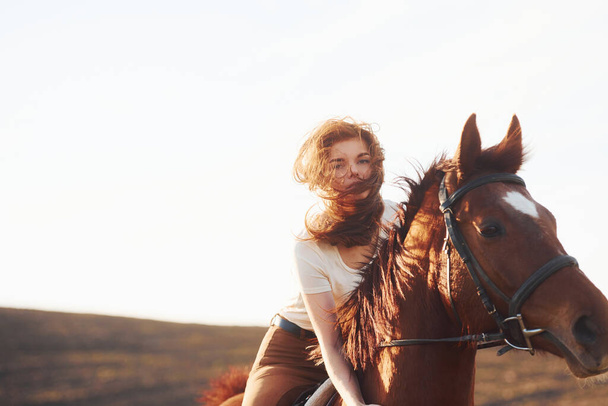 Young woman in protective hat with her horse in agriculture field at sunny daytime. - Foto, imagen