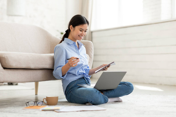 Cheerful young asian woman sitting on floor with laptop - Photo, Image