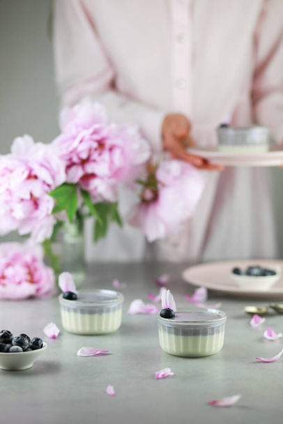 Homemade Italian dessert panna cotta with blue berries and bouquet of peony flowers on gray background.  - Фото, зображення