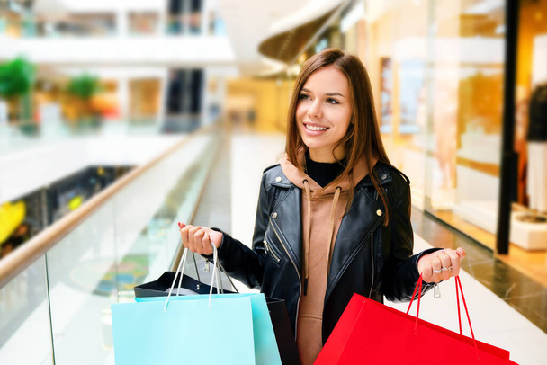 Attractive happy woman with colorful shopping bags in a mall. Blurred background with a free space.  - Photo, Image
