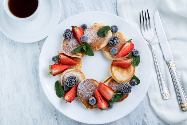 Pancakes with fruit and mint on a white plate, cutlery, a cup of coffee on a light table.Tasty food.Calorie food. - Фото, изображение