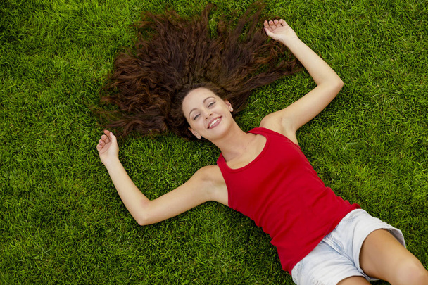 Outdoor portrait of a beautiful young woman lying on the grass - Foto, Imagen