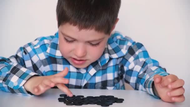 Un niño de 4 años está aprendiendo a contar, enseñando chips de aritmética negra para preescolares. - Metraje, vídeo
