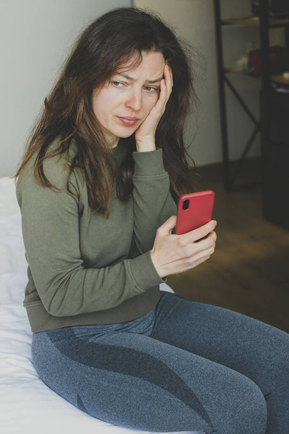 Worried young woman feeling anxiety, holding phone,looking into distance indoor.Waiting for call,thinking about life,relationships problem,unexpected pregnancy,experiencing grief, heartbreak.Vertical - Zdjęcie, obraz
