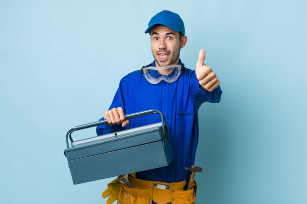 young adult hispanic man feeling proud,smiling positively with thumbs up. toolbox concept and plumber - Zdjęcie, obraz