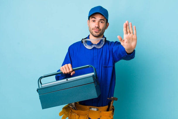 young adult hispanic man looking serious showing open palm making stop gesture. toolbox concept and plumber - Photo, Image