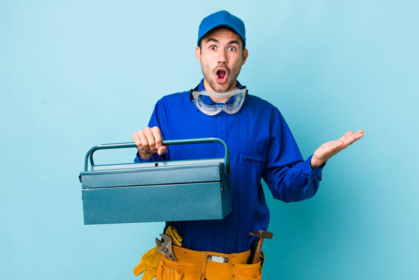 young adult hispanic man amazed, shocked and astonished with an unbelievable surprise. toolbox concept and plumber - Photo, Image